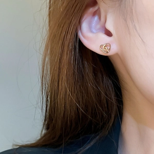 Close-up of elegant gold heart knot stud earring on model with polished metal finish