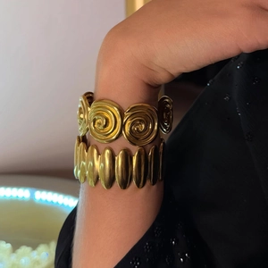 Gold spiral and oval link stainless steel bracelets displayed on a model's wrist