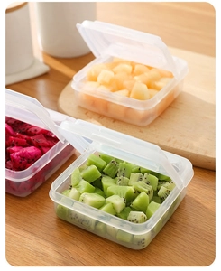 Three square plastic food storage boxes with lids filled with fresh diced fruit on wood