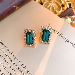 Macro shot of rectangular gold earrings with a green gemstone and zircon details