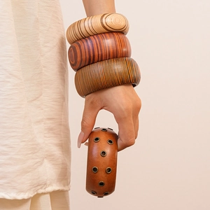 Detail of stacked wide wooden bracelets with natural textures and metal stud accents