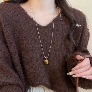 Détail du collier avec pendentif cœur en œil de tigre sur un pull en maille marron