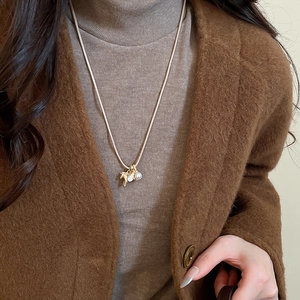 Détail du collier pendentif cheval avec perle sur pull beige et manteau brun