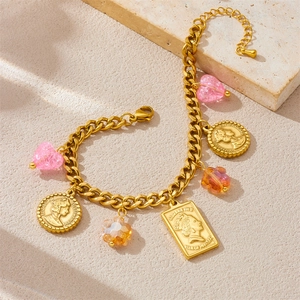 Detailed view of gold Cuban chain bracelet with pink heart and coin pendants on stone