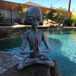 Detailed view of grey meditating alien resin figurine sitting by a garden pond