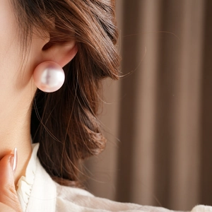 Close-up of a large pink pearl stud earring worn by a model with soft lighting