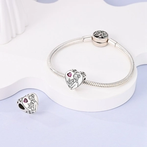 Detailed macro view of heart charm with mother-child engraving and red gem on silver bracelet