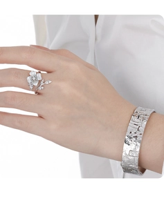 Detail shot of a silver floral open ring and a textured wide cuff bracelet on a model