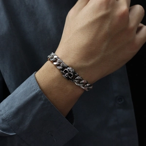 Close-up of a stainless steel Cuban chain bracelet with a skull pendant on male wrist