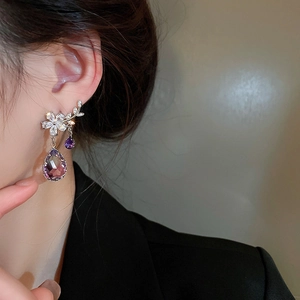 Close-up of elegant flower stud earrings with purple crystal teardrop pendants on model