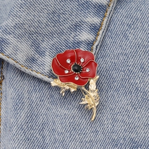Detail of red enamel poppy brooch with crystal accents on denim jacket collar