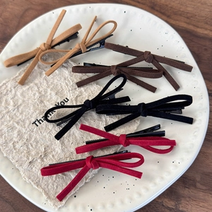 Detail of suede bow hair clips in khaki, brown, black and wine red on a vintage plate