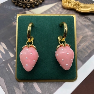 Pink strawberry earrings with white dots and gold leaves on a vintage velvet stand