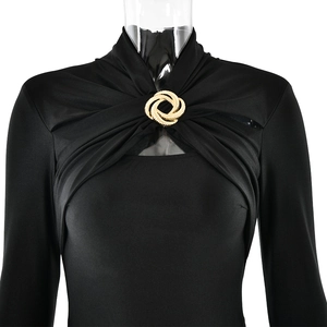 Detail of black long sleeve dress featuring a central twist knot and a golden metal brooch