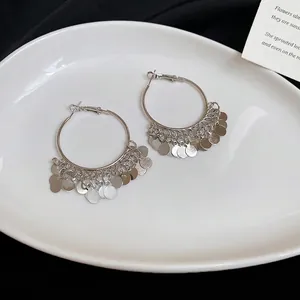 Elegant silver hoop earrings with layered metal sequin tassels on white ceramic plate