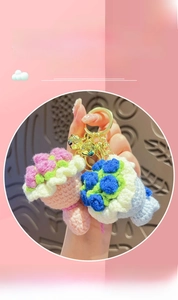 Close-up of hand holding pink and blue crochet bouquet keychains with small bells