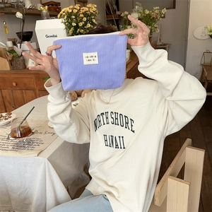 Close-up of light purple corduroy makeup bag with white label in a cozy cafe setting