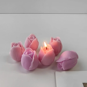 Close-up of pink tulip-shaped candles with one lit flame on a minimalist background