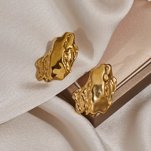 Detailed view of golden irregular lava texture earrings on luxury champagne satin fabric