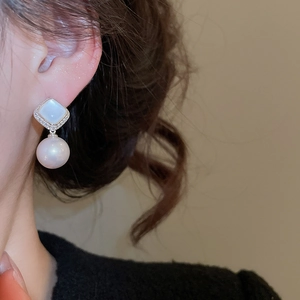 Macro detail of elegant pearl drop earrings with mother-of-pearl stud and zircon border