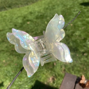 Macro shot of iridescent acetate butterfly hair claw clip reflecting pastel colors on a branch