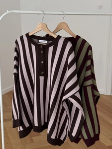 Close-up of striped knit sweaters with half-button collars on wooden hangers in a room