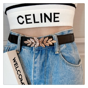 Detail of a slim black elastic belt featuring a golden leaf buckle on high-waist jeans