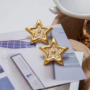 Détail de boucles d'oreilles étoile dorées avec strass brillants sur fond de magazine