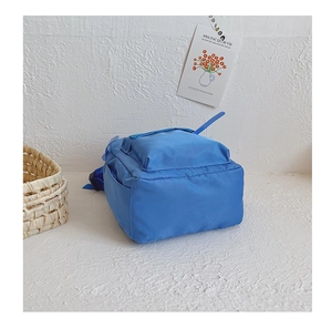 Minimalist blue kindergarten backpack for toddlers against a white textured wall
