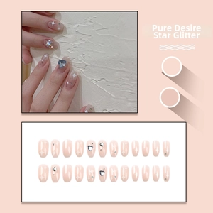Detail of nude pink press-on nails featuring white stars and blue heart-shaped rhinestones