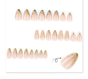 Close-up of nude pink press-on nails with 3D gold wave borders and bow decorations