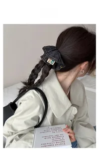 Detail of dark blue denim scrunchie with yellow stitching on twin braids hairstyle