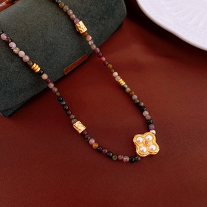 Detailed close-up of golden clover pendant with white pearls and colorful beads necklace