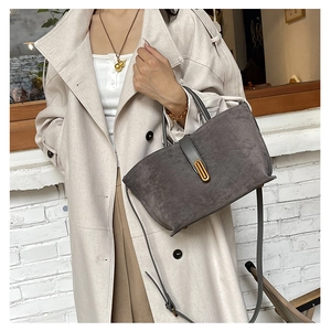 Detail view of charcoal suede bucket bag with gold oval buckle on a beige trench coat