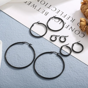 Set of four matte black stainless steel hoop earrings in various sizes on a blue texture