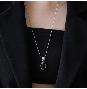 Macro view of minimalist silver necklace with oval black resin pendant on model