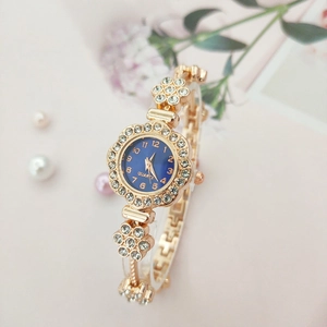 Detail of gold floral watch with blue dial and crystals on an elegant pink background