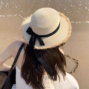 Detail of beige woven straw hat with black bow and fringe brim on a sunny beach