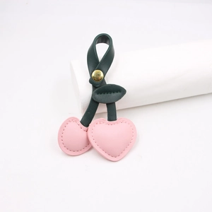 Detail of pink heart-shaped cherry leather keychain with green leaves and gold buckle