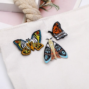 Gros plan de broches papillon et mite en émail vintage sur un sac cabas en toile