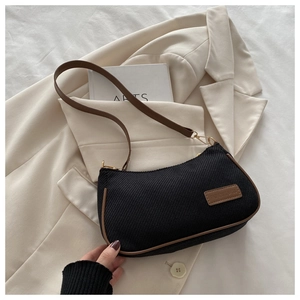 Detail view of black canvas underarm bag with brown leather trim and retro rectangular label