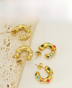 Detail of C-shaped hoop earrings with clear and colorful rhinestones on stone background