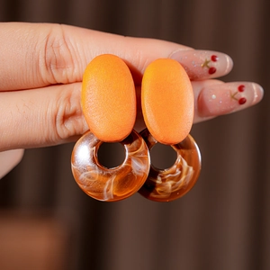 Close-up of geometric resin earrings with orange oval stud and marble pattern ring