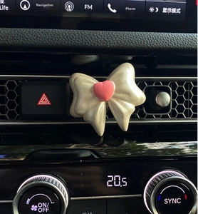 Car air vent clip featuring a pearlescent white bow design with a pink 3D heart detail