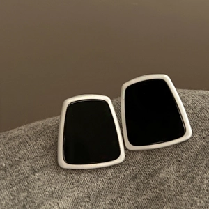 Close-up of black trapezoid resin earrings with silver metal edges on grey knitwear