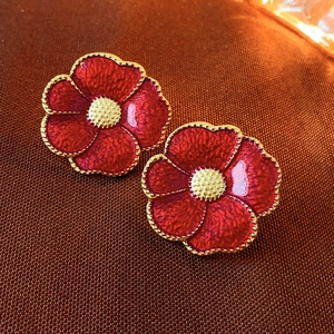 Macro detail of red enamel flower earrings with golden core on vintage checkered fabric