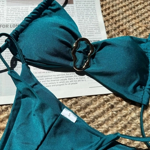 Nahaufnahme des dunkelgrünen Bikini-Oberteils mit glänzendem Stoff und goldenem Metallring