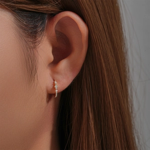 Close-up of gold-plated silver huggie hoop earring with flower-shaped zircons on ear