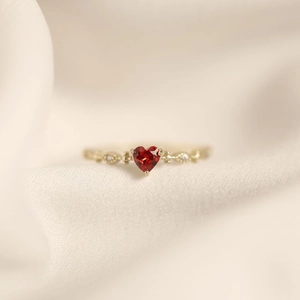 Macro view of heart-shaped ruby ring with gold filigree and diamond accents on silk