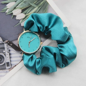 Detail of teal satin ribbon watch strap and gold round dial on a floral background